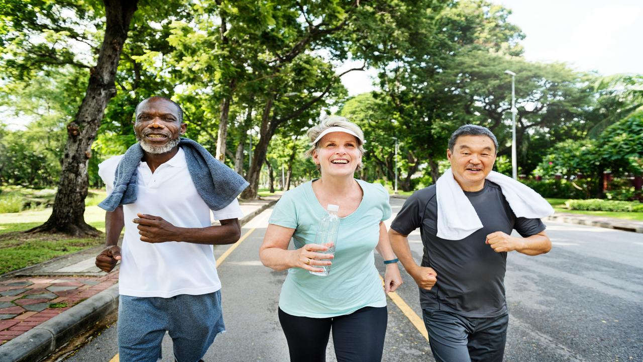 A group of three older adults jogging together in a sunny park.