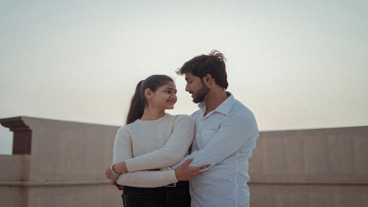A couple embracing and smiling on a rooftop at sunset.