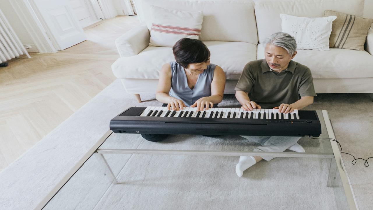 A couple sitting on the floor, playing a digital piano together in a cozy living room.