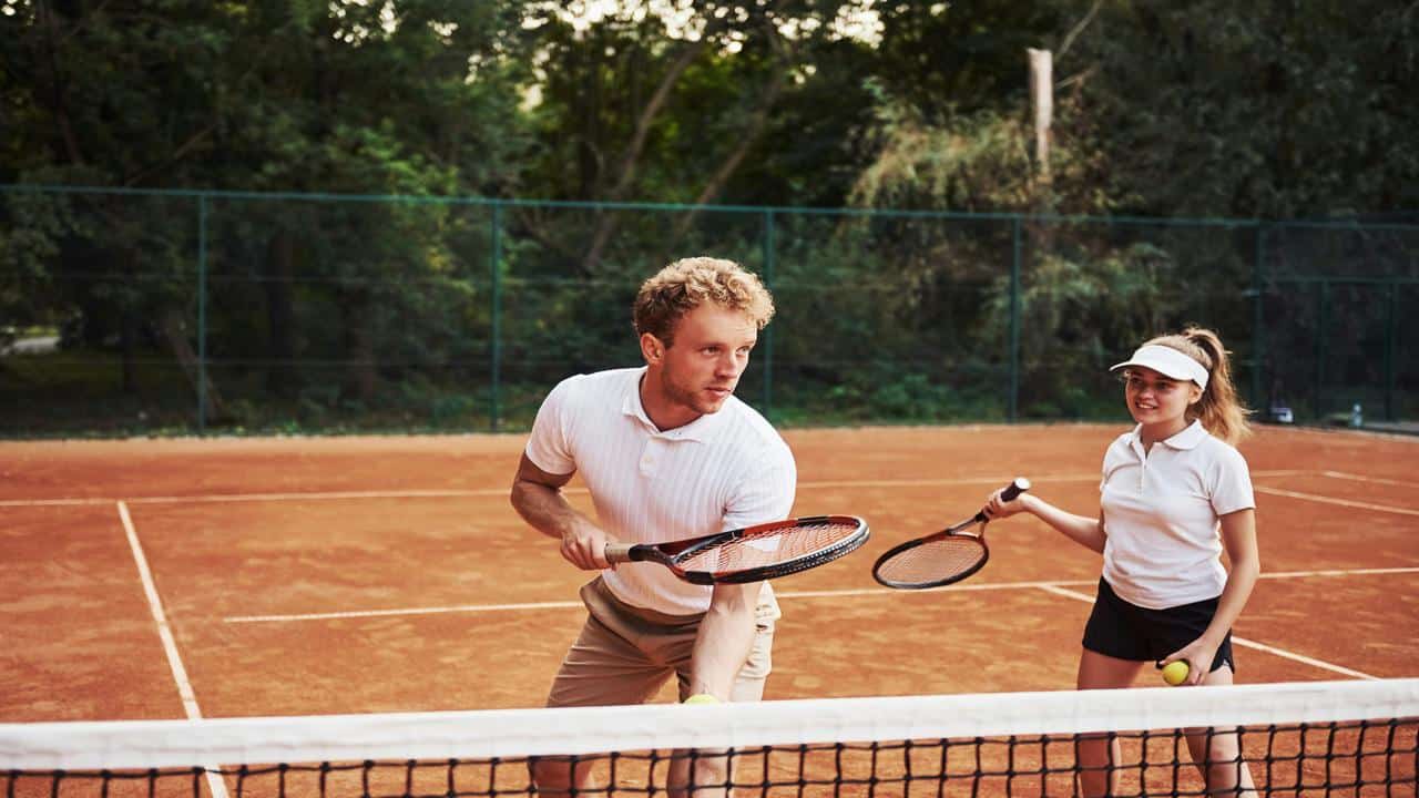 A man teaching a woman tennis on a clay court.