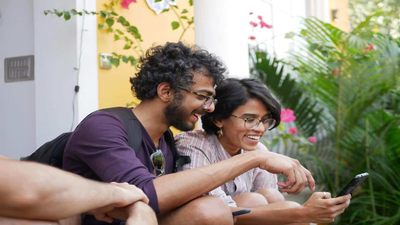 A smiling couple sitting outside, looking at a smartphone together.