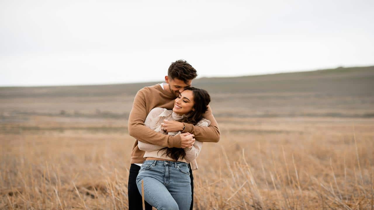 A couple embracing and smiling in a dry open field.