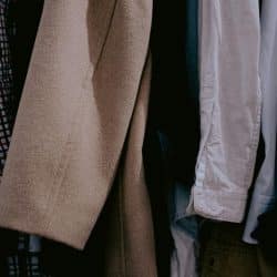 A row of men's clothing hanging in a closet, including shirts, jackets, and a beige overcoat.