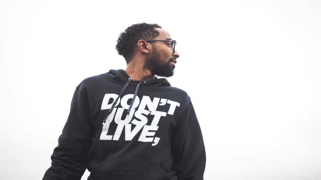 A man in glasses wearing a black hoodie with the text "DON'T JUST LIVE,".