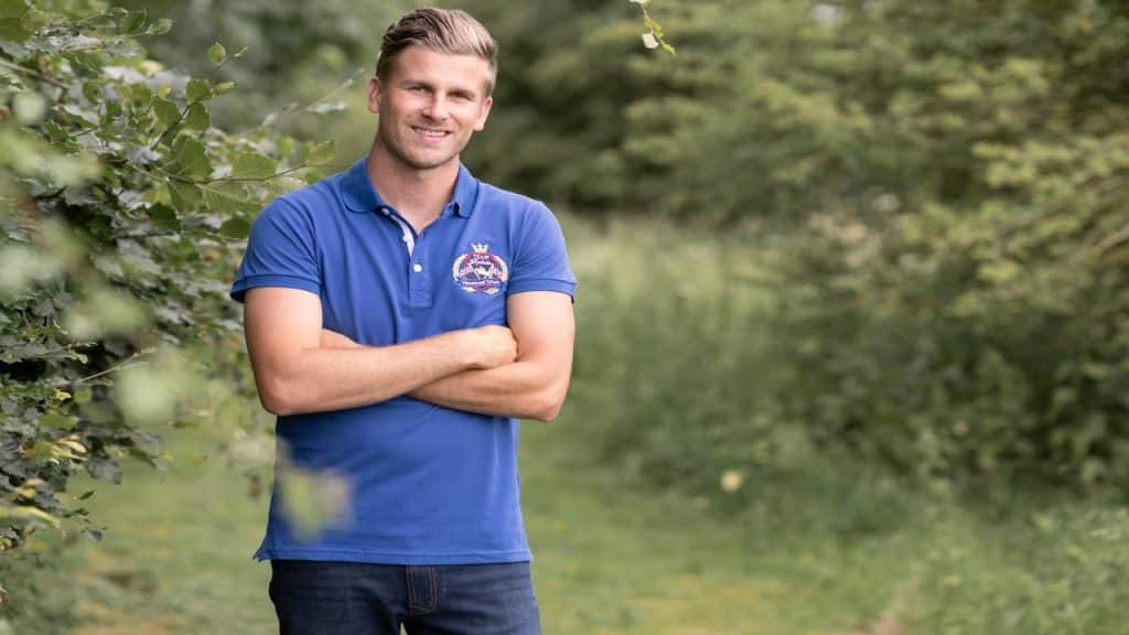 A man in a blue polo shirt standing outdoors with arms crossed, smiling.