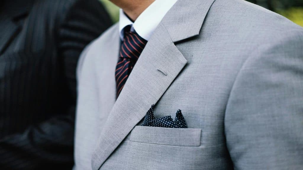 A man in a light gray suit with a striped tie and polka dot pocket square.