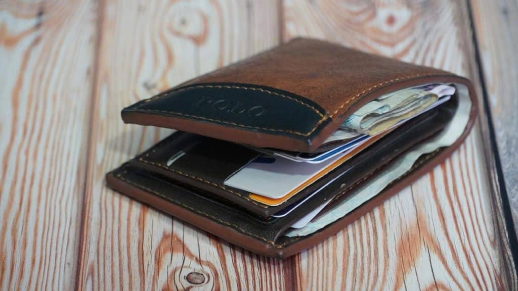 A brown leather wallet filled with cash and cards, resting on a wooden surface.
