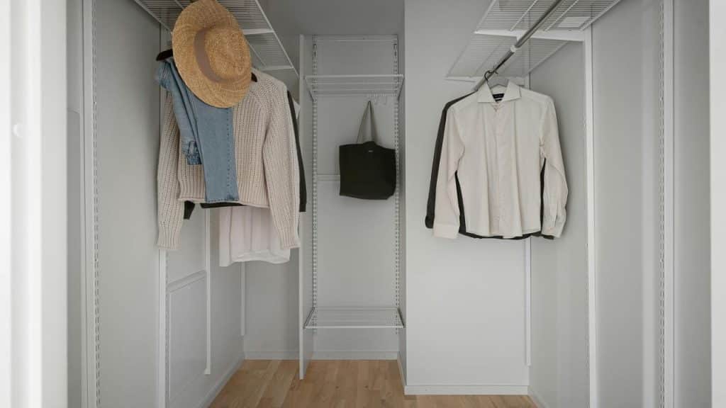 A minimal walk-in closet with a few hanging clothes, a straw hat, and a tote bag.