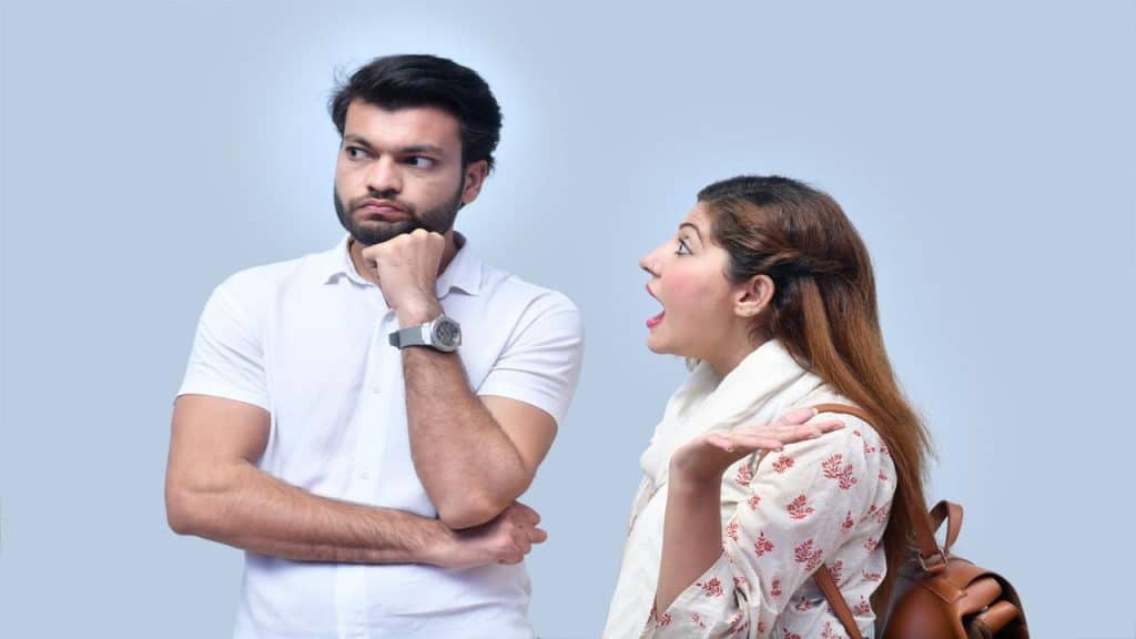 A frustrated woman argues with a man who looks away with a bored expression and crossed arms.