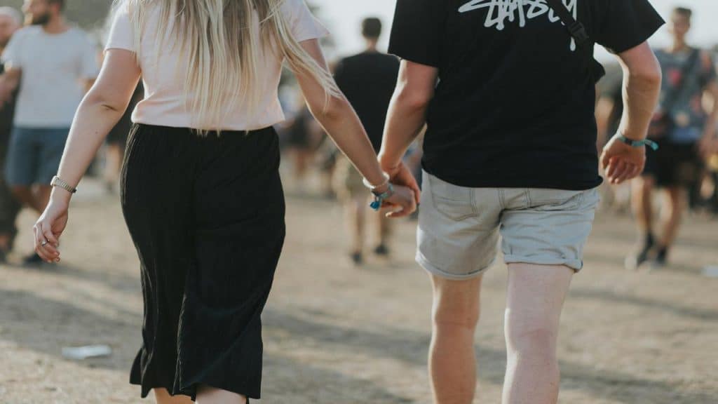 A couple walks hand in hand through a crowded outdoor event, seen from behind.