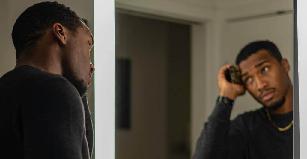 A man reflects in the mirror with a serious expression, confronting personal expectations.