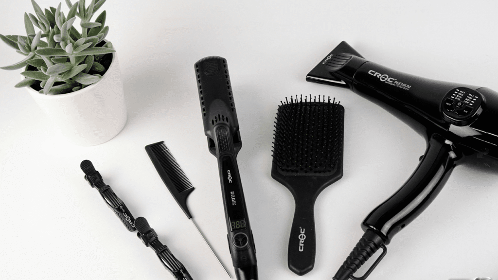 A set of black hair styling tools and a plant on a white surface.