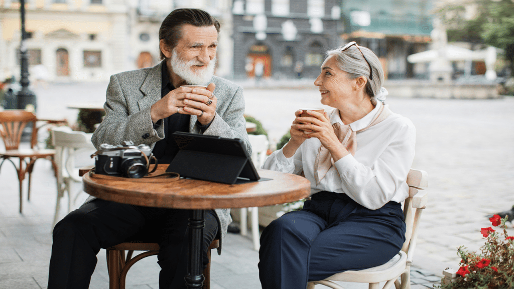 A stylish older couple enjoys coffee and conversation at an outdoor café.