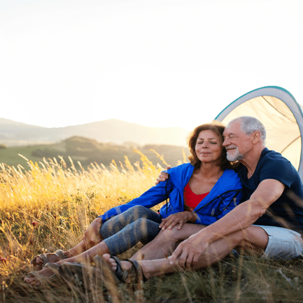 An older couple sitting together outside a tent in a grassy field at sunset.