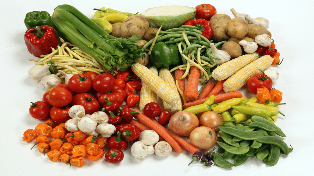 A colorful assortment of fresh vegetables, including tomatoes, carrots, corn, potatoes, bell peppers, onions, garlic, mushrooms, and various beans.