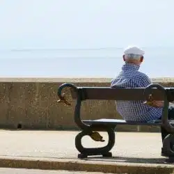 An old man sitting at a bench looking at the sea