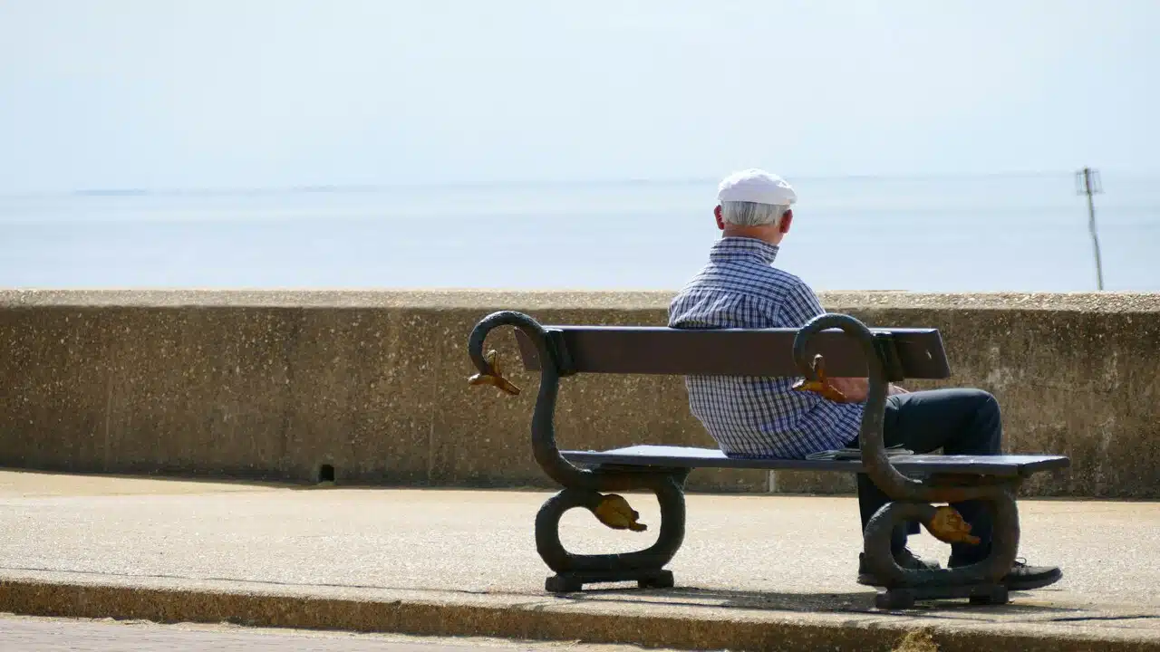 An old man sitting at a bench looking at the sea