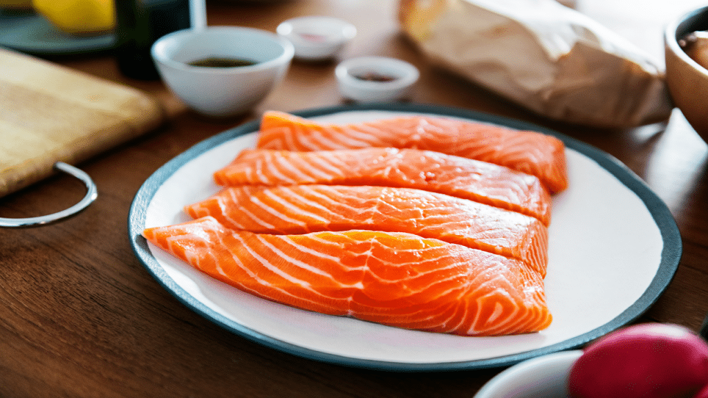 A plate of raw salmon fillets on a wooden table.