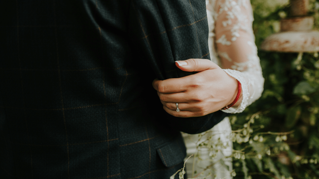 Close-up of a bride holding onto the groom’s suit arm, highlighting her engagement ring.