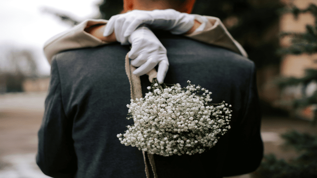 A bride in white gloves hugs her groom from behind, holding a bouquet.