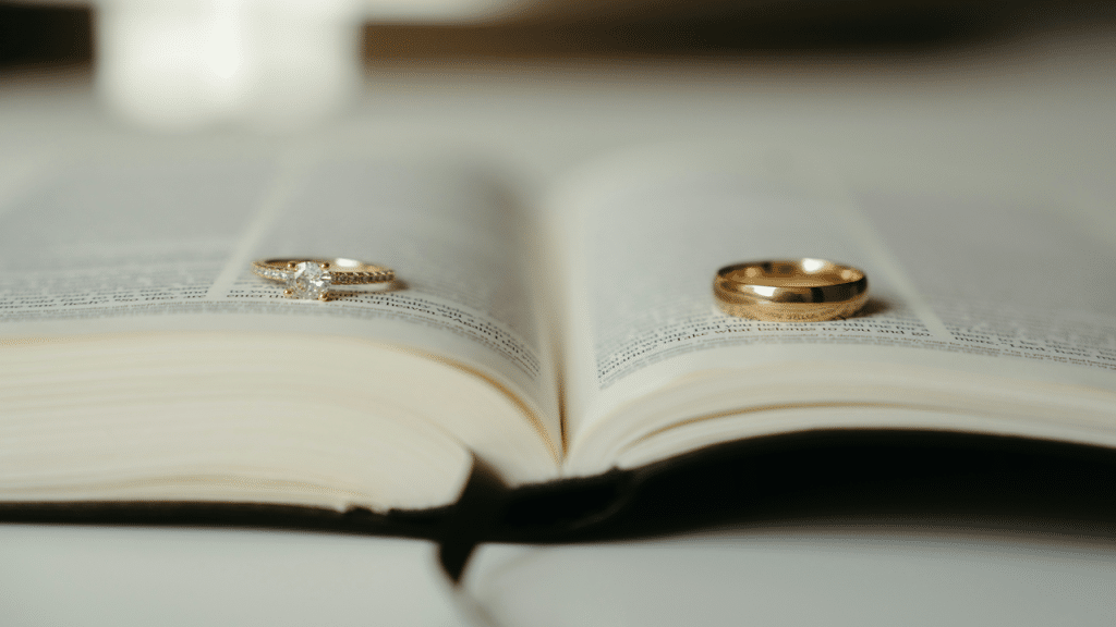 A diamond engagement ring and a gold wedding band rest on the pages of an open Bible.