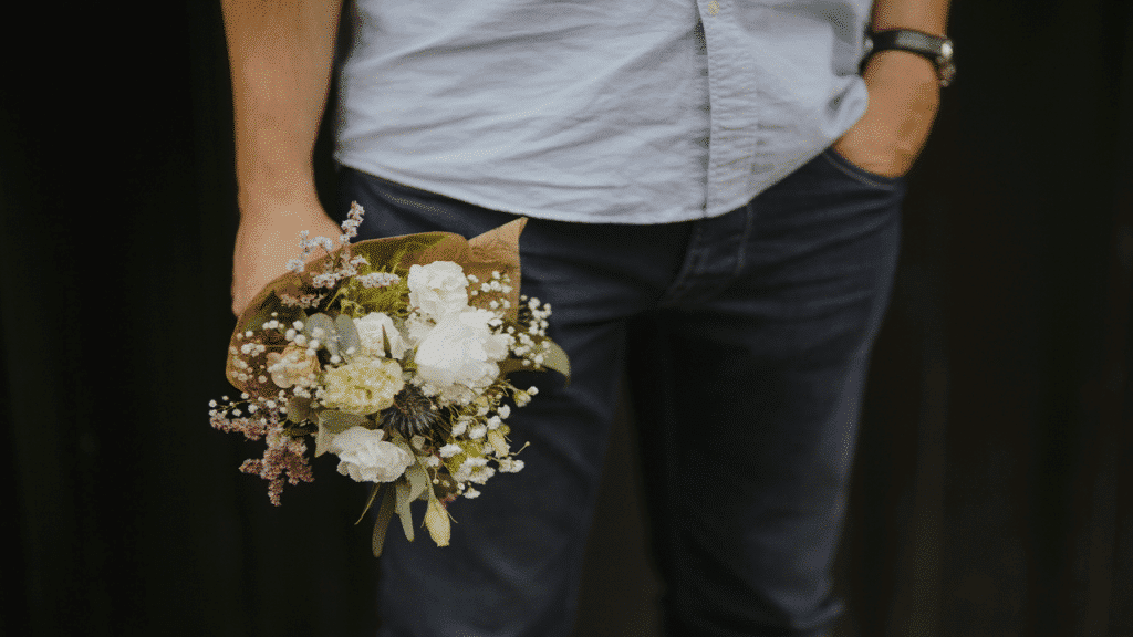 A casually dressed man holds a small bouquet of flowers
