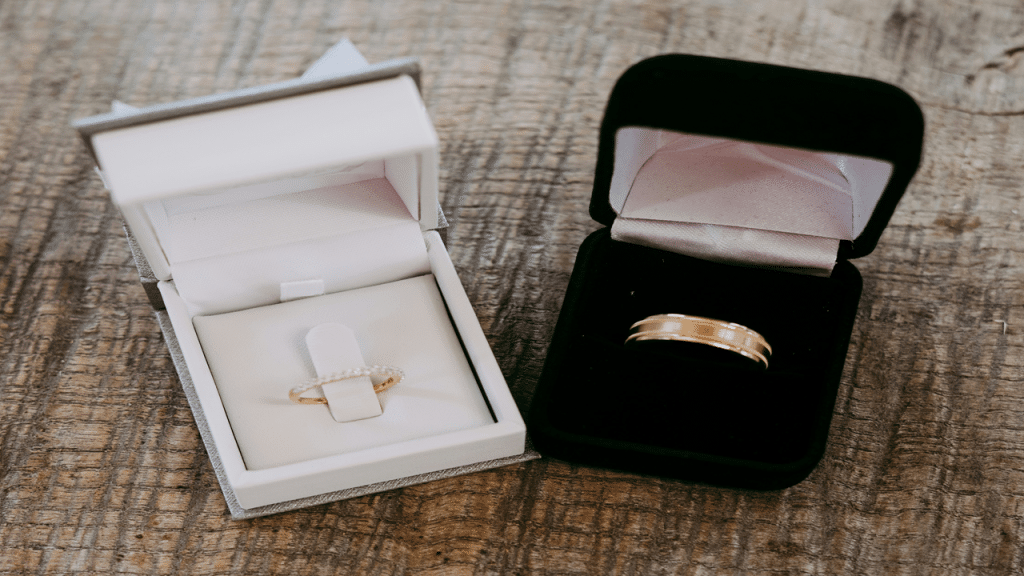 Two wedding rings are in open ring boxes on a wooden surface.
