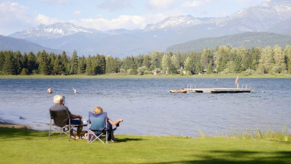An old couple sitting on a lakeside enjoying the mountain view.