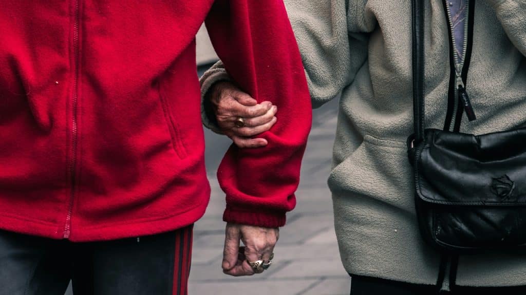 An old couple holding arms while walking together.