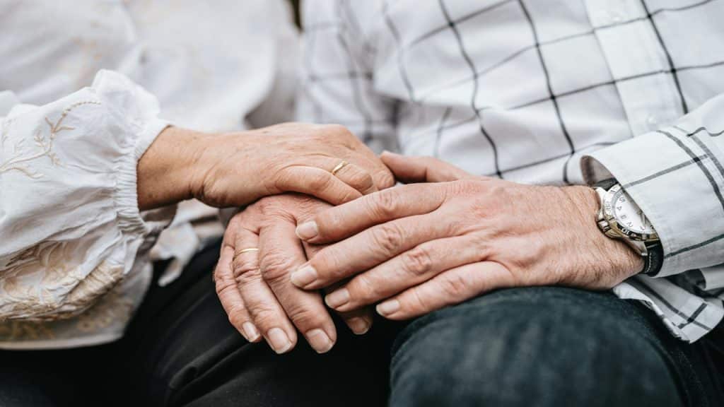 A close-up photo of an old couple holding hands.