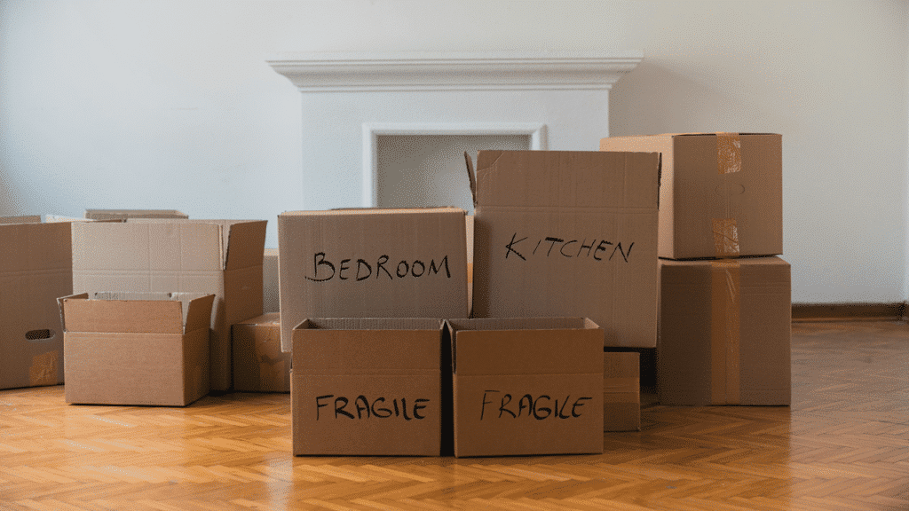 A stack of labeled cardboard boxes sits on a wooden floor, ready for moving into a new home.
