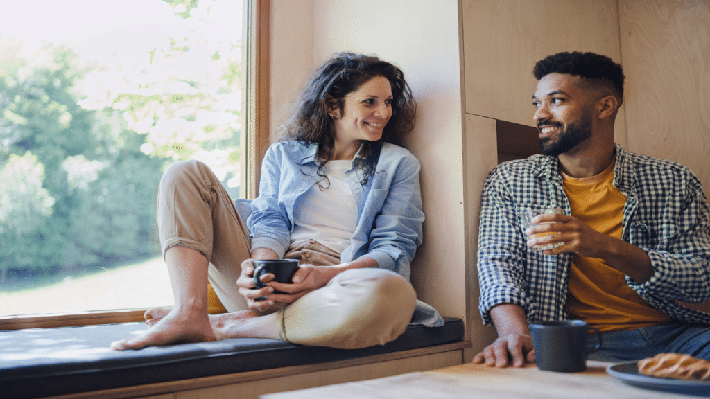 A smiling couple talking over drinks by a window.