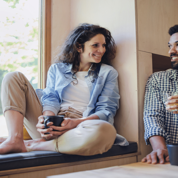 A smiling couple talking over drinks by a window.