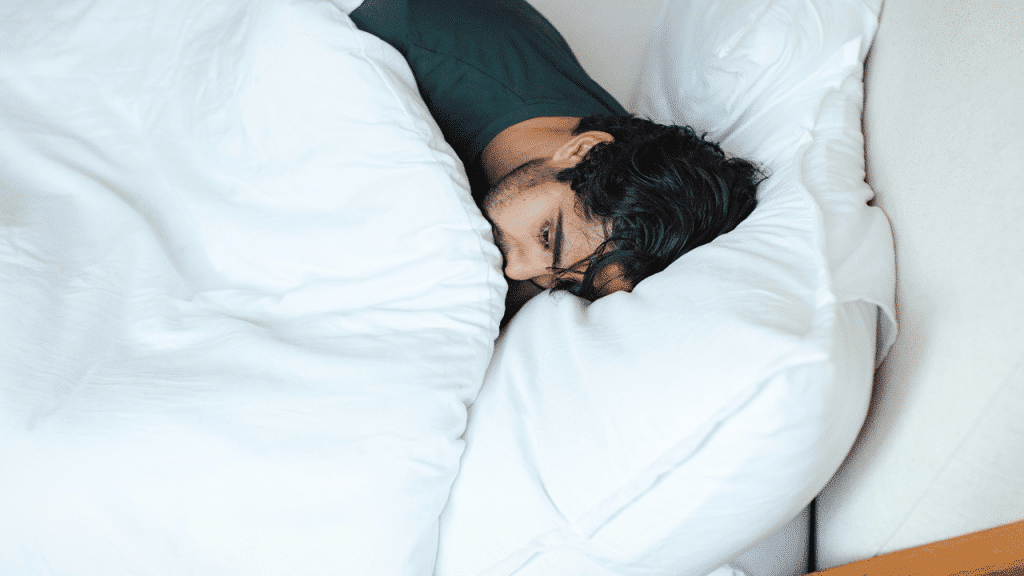 A man resting in bed with his head on a pillow.