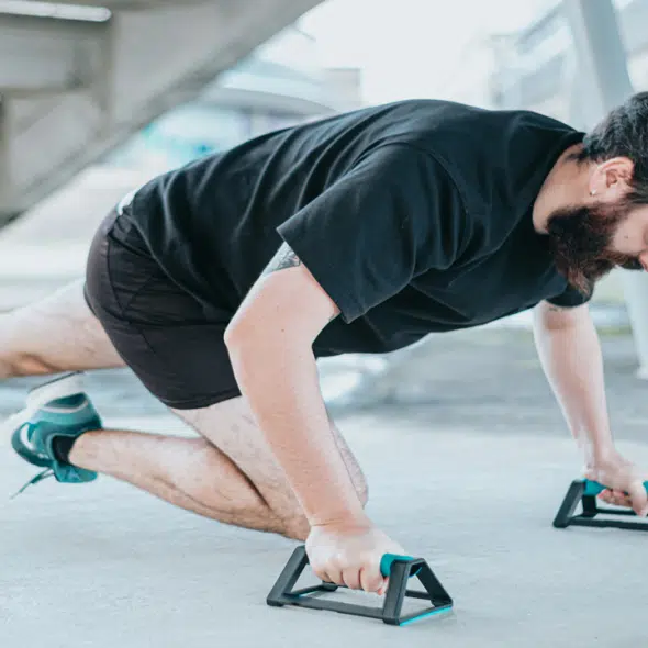 A man performing mountain climbers with push-up bars on a concrete surface outdoors.