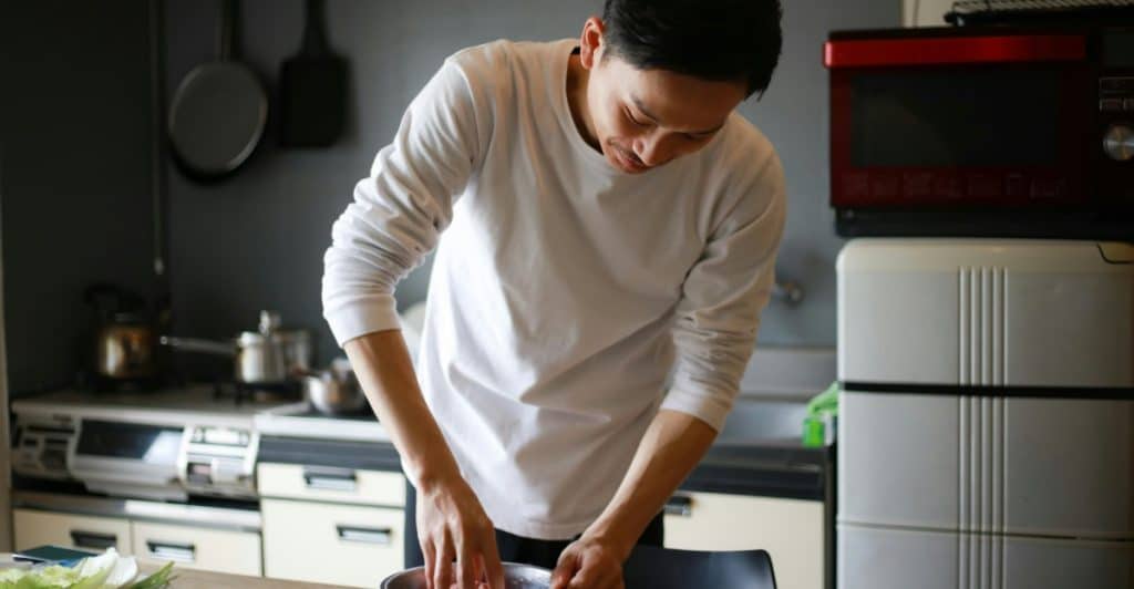 A man in a white shirt mixes ingredients in a bowl in a kitchen.