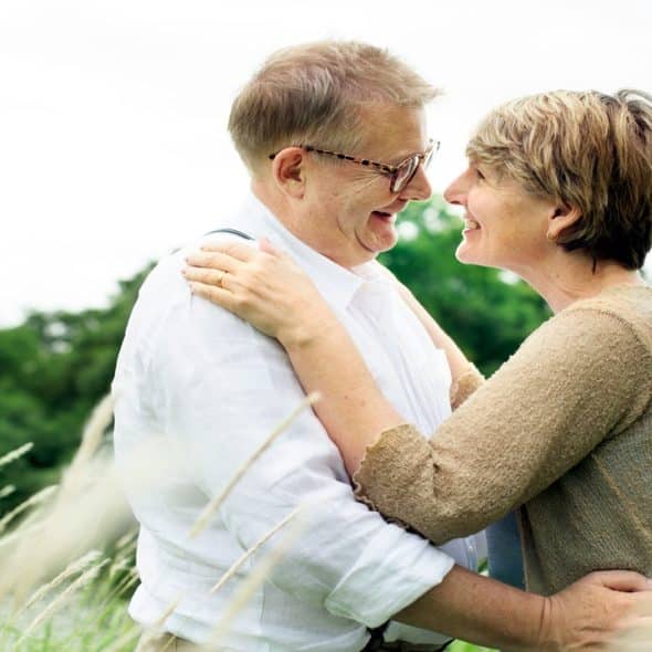 An old couple dancing together on a grass field.