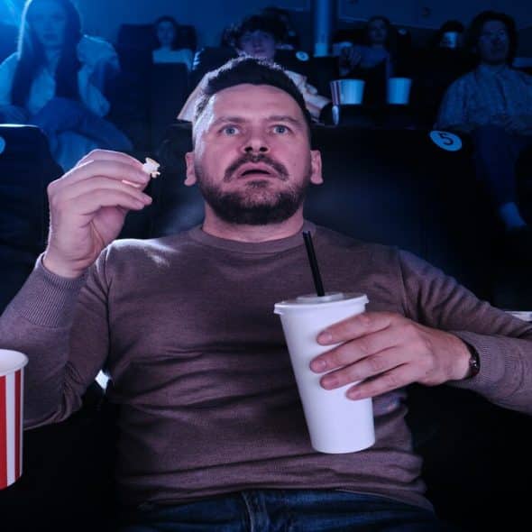 A man looking scared while watching movie at the cinema.