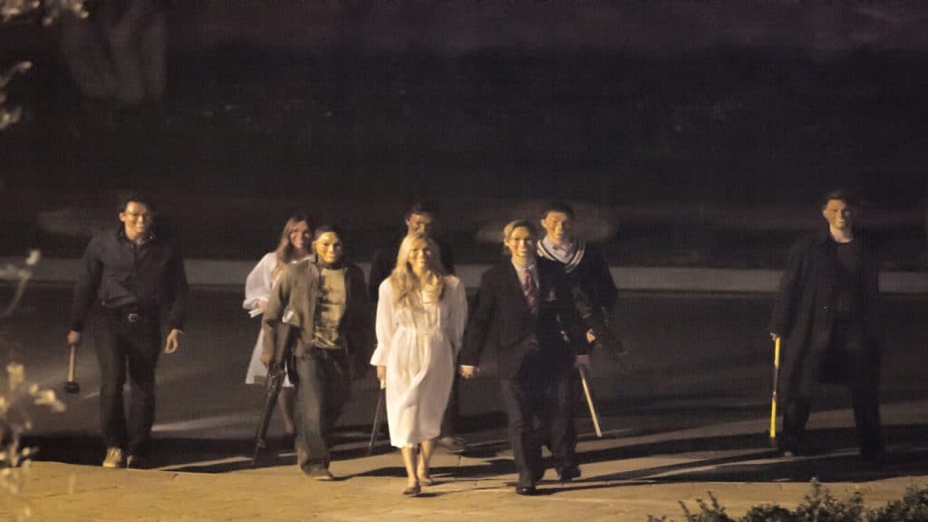 A group of people wearing masks and holding clubs walking down a dark street.