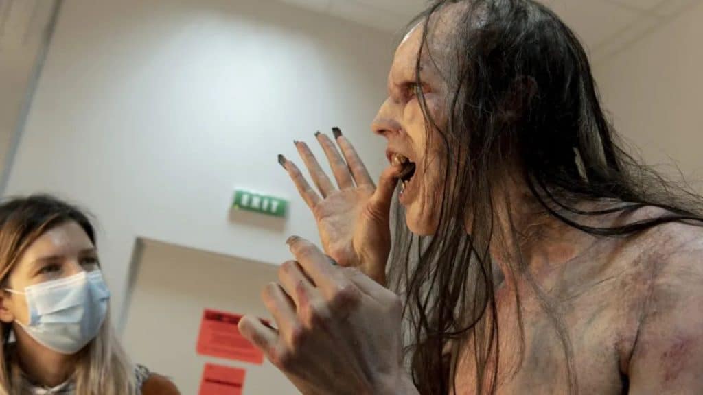 A creature with biting its thumb while a woman wearing a mask watches.