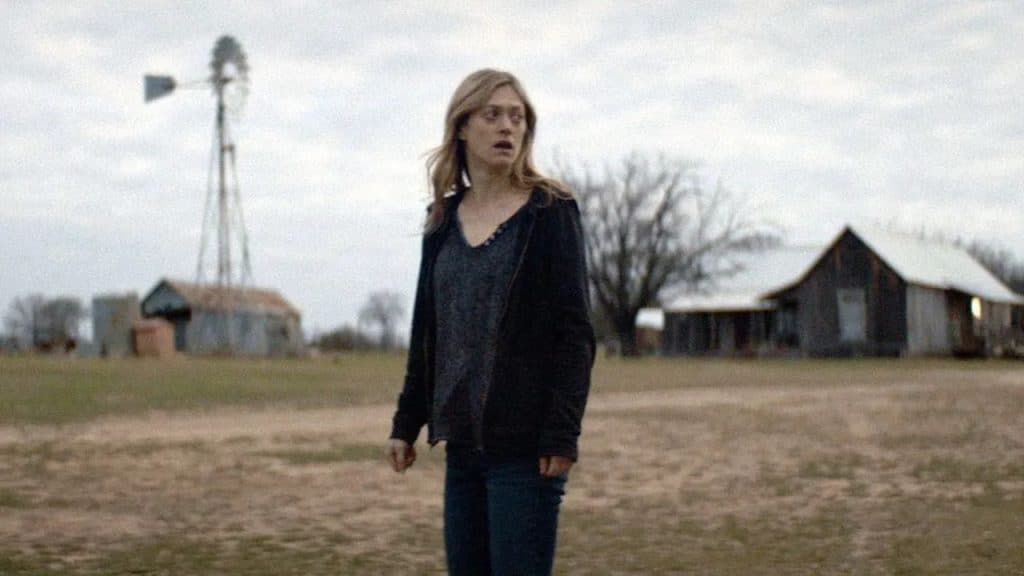 A woman standing in a field, looking sideways while appearing distraught.