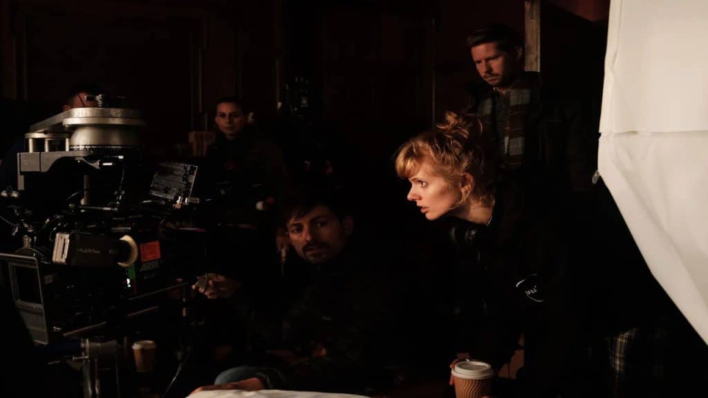 A woman talking to a cameraman with some people in a dark background.