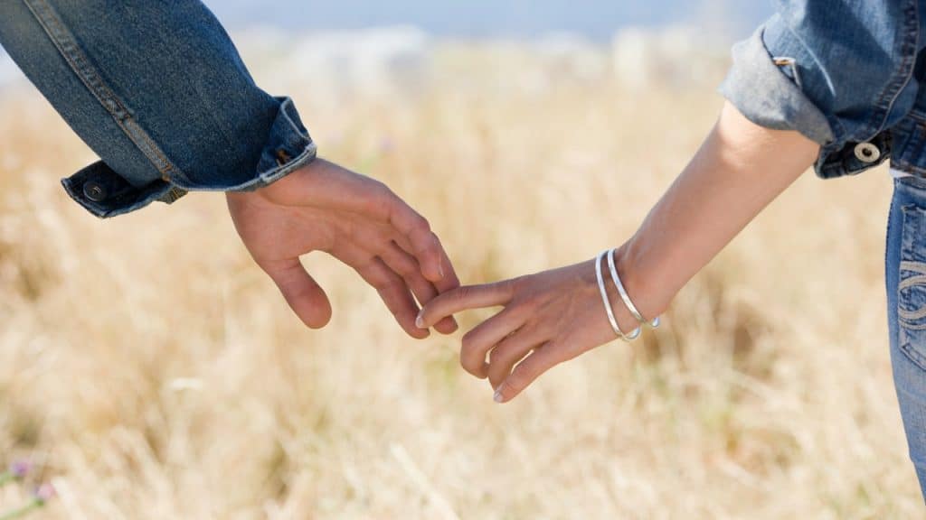 A couple holds hands in a grass field.