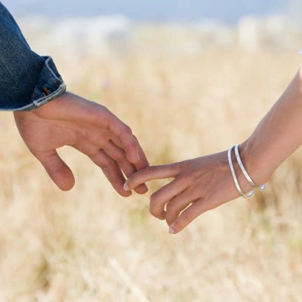 A couple holds hands in a grass field.