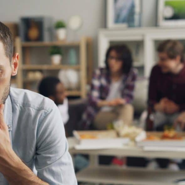 A man sitting calmly and reflecting in a peaceful indoor setting with friends at his back.