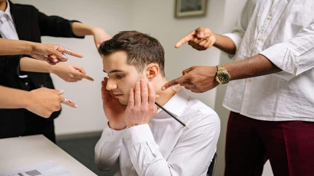A man trying to cover his ears from a draining social dynamic, honoring his emotional limits.