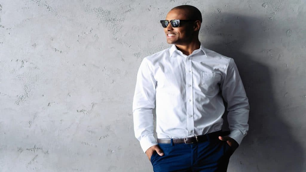 A man wearing a button-up shirt standing against a wall.