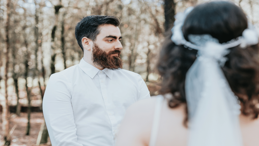 A groom gazes at his bride during an outdoor forest wedding.