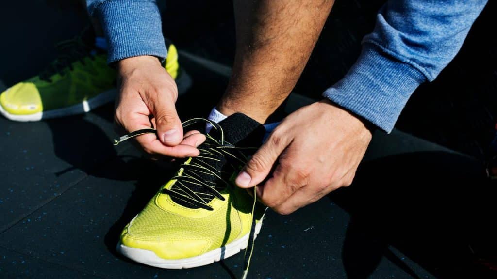 A close-up of a person tying the laces on a bright yellow and black sneaker while wearing a blue sweatshirt.