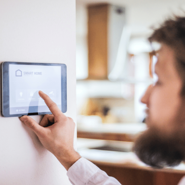 A man using a wall-mounted touchscreen display to control a smart home system.
